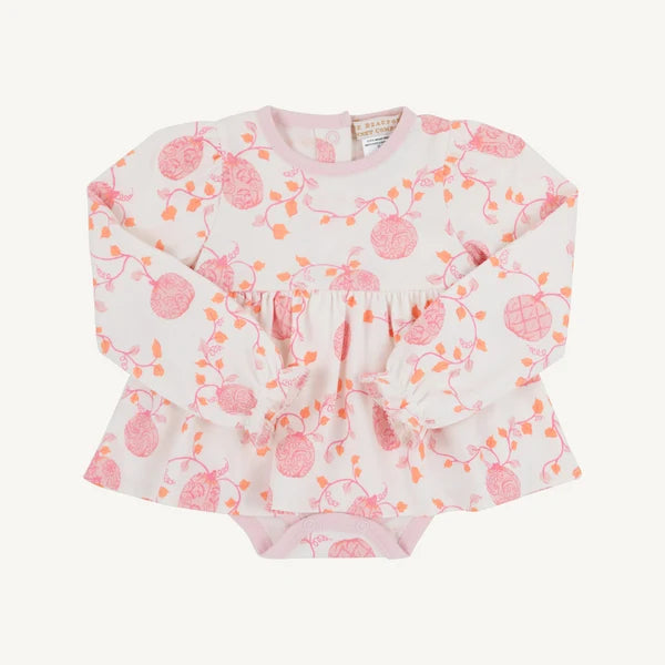 A baby long-sleeve top with a pink and orange berry vine pattern on a white background, featuring a ruffled peplum waist and tie detail, laid flat on a light cream background.