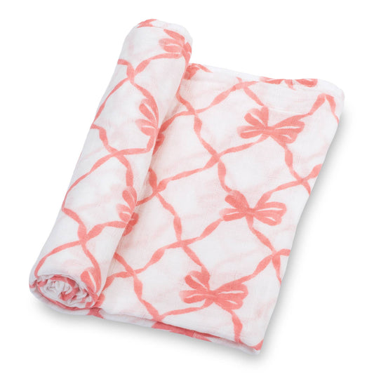 A folded white muslin blanket with a coral pink bow and lattice pattern, shown rolled on a clean white background.