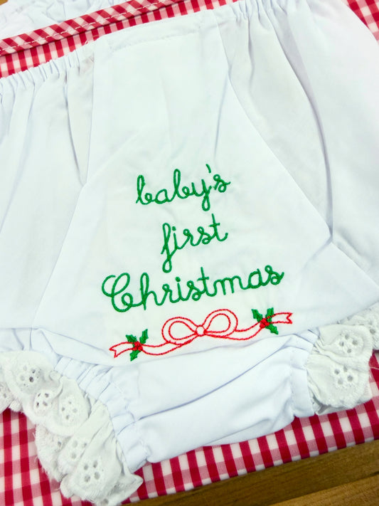 White baby bloomers with 'baby's first Christmas' embroidered in green and red, featuring a red bow and holly design background.