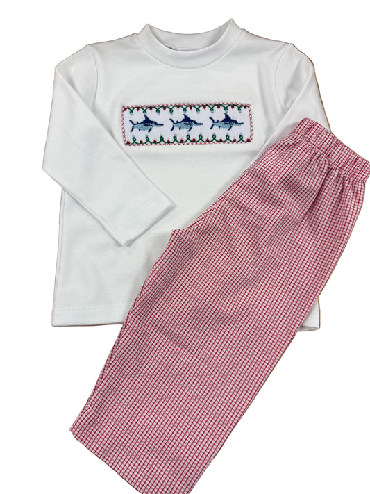A children's two-piece pajama set laid flat on a wooden floor, featuring a white long-sleeve top with a smocked chest panel of blue marlin and red/green trim, paired with pink and white gingham pants.