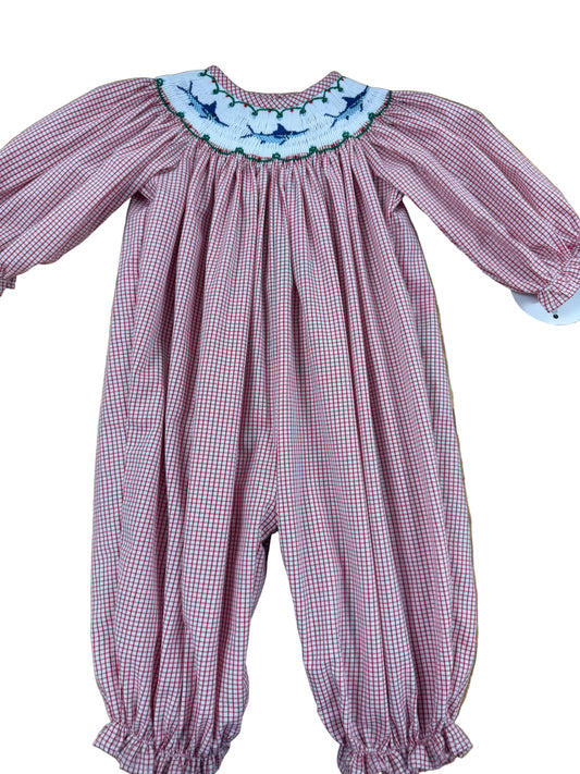 A baby smocked romper in a pink and white gingham pattern, featuring a white floral embroidered collar with blue and green accents, laid flat on a wooden floor.