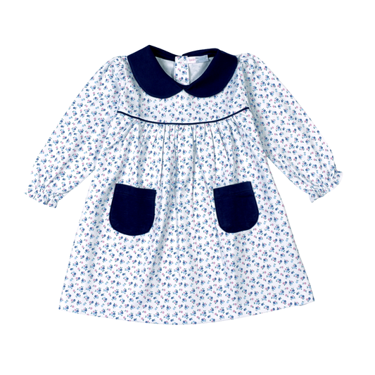 A long-sleeve baby dress with a white background, blue floral print, and dark navy blue collar, trim, and pockets.