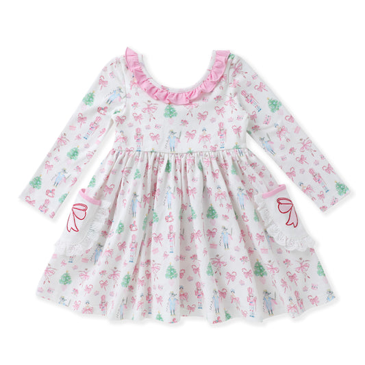 A long-sleeve baby dress with a white base, decorated with a pink and green fairy and bow pattern. It features a pink ruffled neckline, a gathered waist, and lace details on the sleeves and hem.