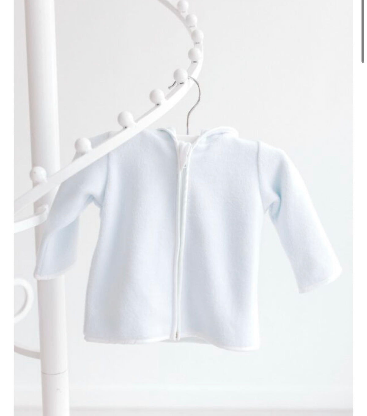 A light blue long-sleeve zip-up hoodie for dolls, hanging on a white decorative clothing rack against a white background.