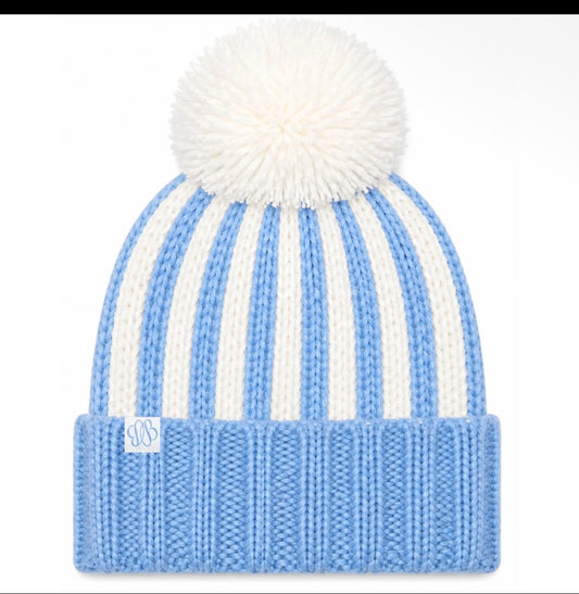 A light blue and white striped knit beanie hat with a fluffy white pom-pom on top and a folded ribbed cuff featuring a small white monogram patch.