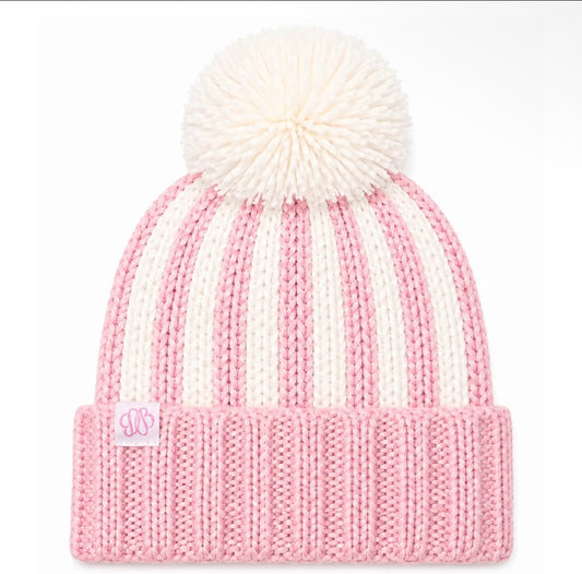 A pink and off-white striped knit beanie with a large white pom-pom on top and a ribbed cuff featuring a small pink monogram patch.