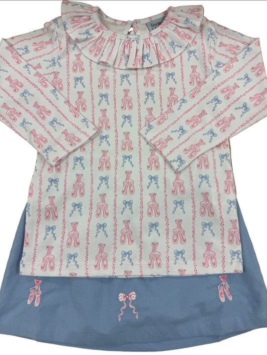 A children's long-sleeve top with a ruffled collar, featuring an all-over vertical pattern of pink and blue ballet pointe shoes on a light cream background, layered over a dusty blue skirt.
