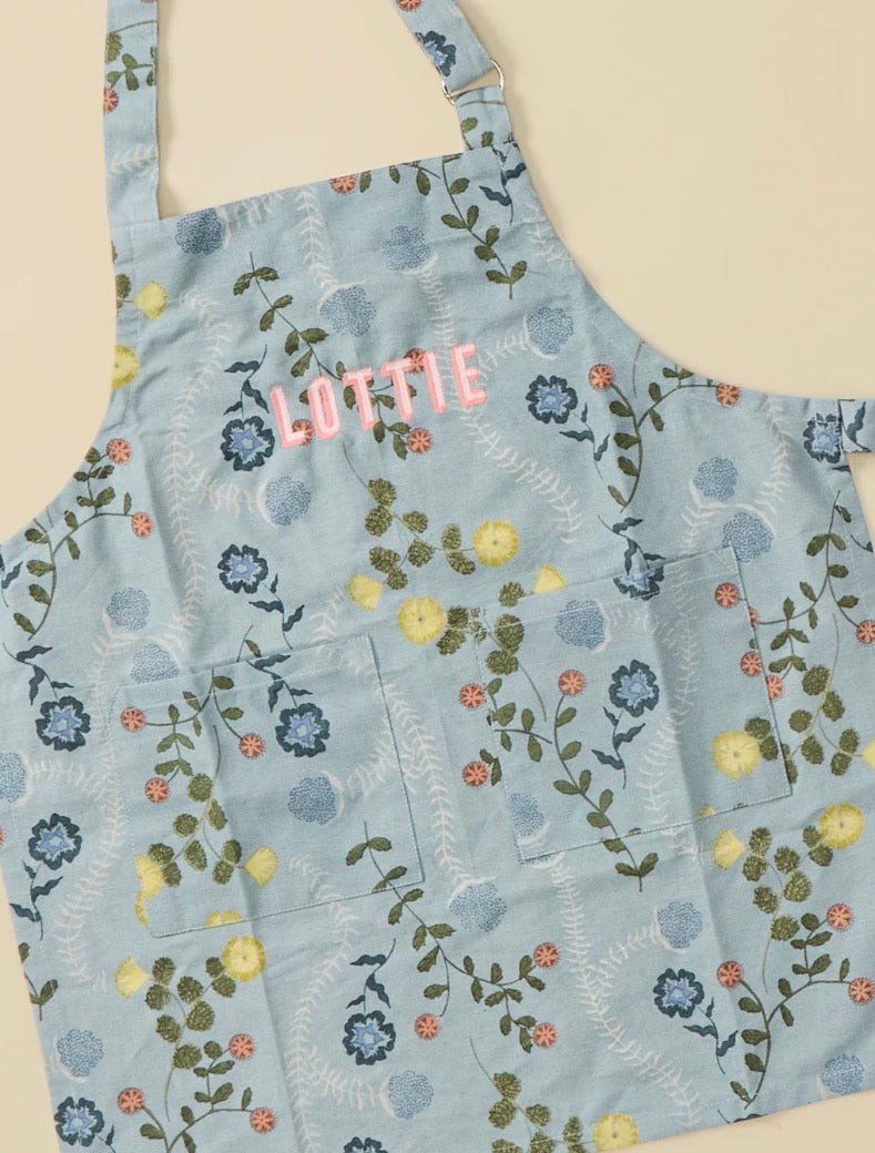 A light blue apron with a floral pattern of yellow, blue, and pink flowers and green vines.