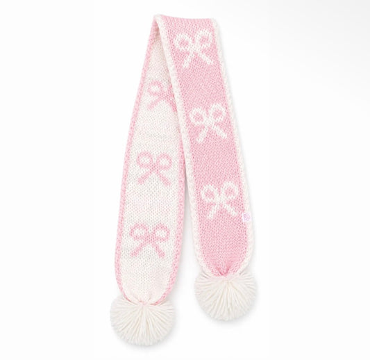 A pink and white knit scarf with white pom-poms on both ends, featuring a repeating bow pattern.