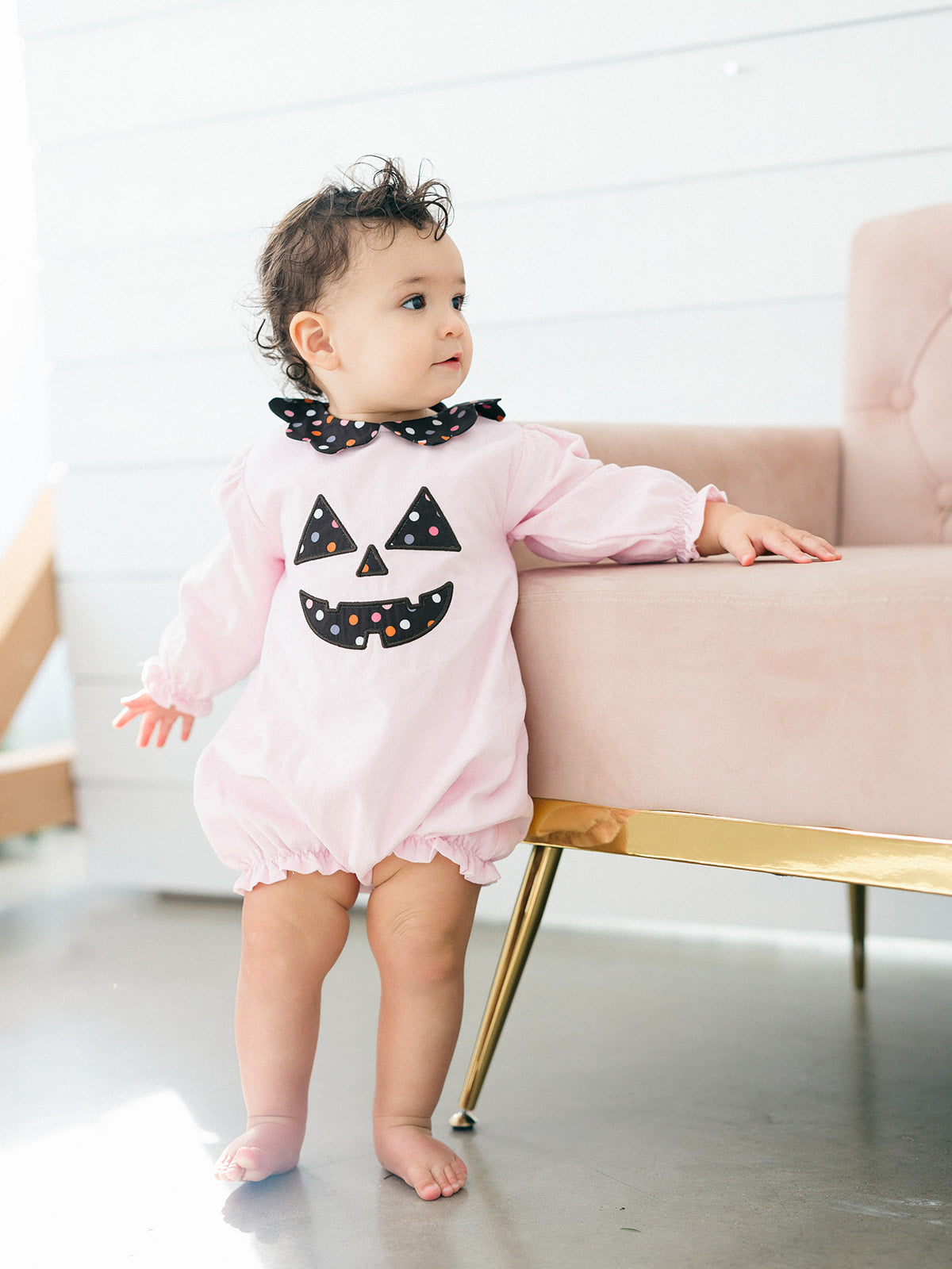 tpink long-sleeve romper with a black polka-dot Peter Pan collar and a black jack-o'-lantern face applique on the chest cordoroy