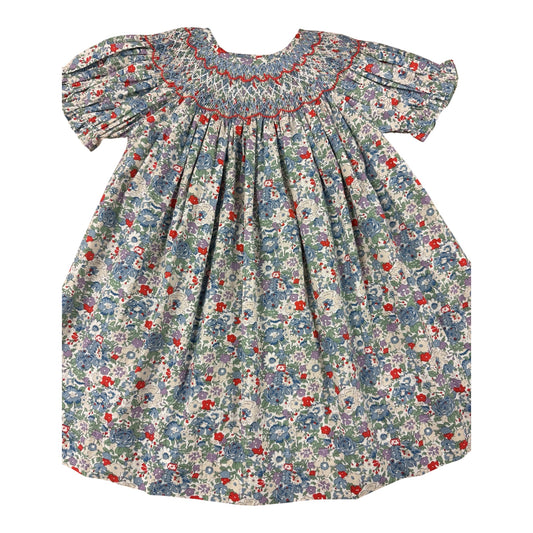 A baby girl's smocked dress with short puff sleeves, featuring a blue, red, and white floral print on a light background.