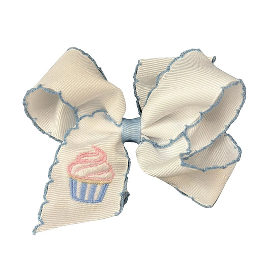 White grosgrain hair bow with a blue moonstitch edge and a pink and blue embroidered cupcake.