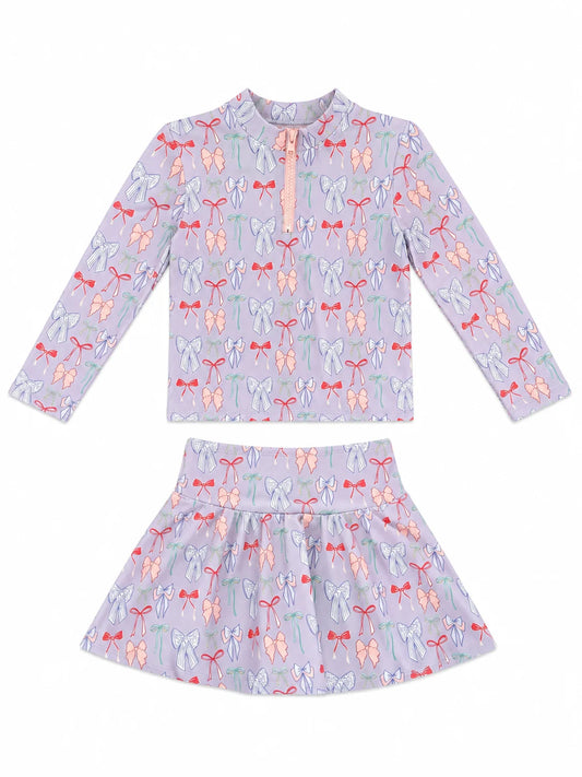A two-piece girls' swim or lounge set featuring a long-sleeve mock-neck top and a matching flared skirt, both in a light lavender-purple color with an all-over bow  print in pink, orange, and green, displayed on a clean white background.