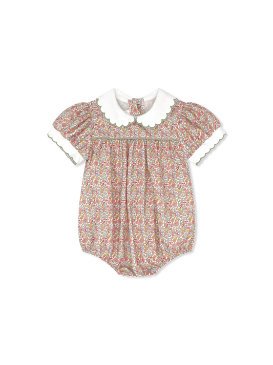A baby romper with a dense multicolor floral print on a light pinkish-beige base, featuring a contrasting white Peter Pan collar and white ruffled short sleeves with green trim.