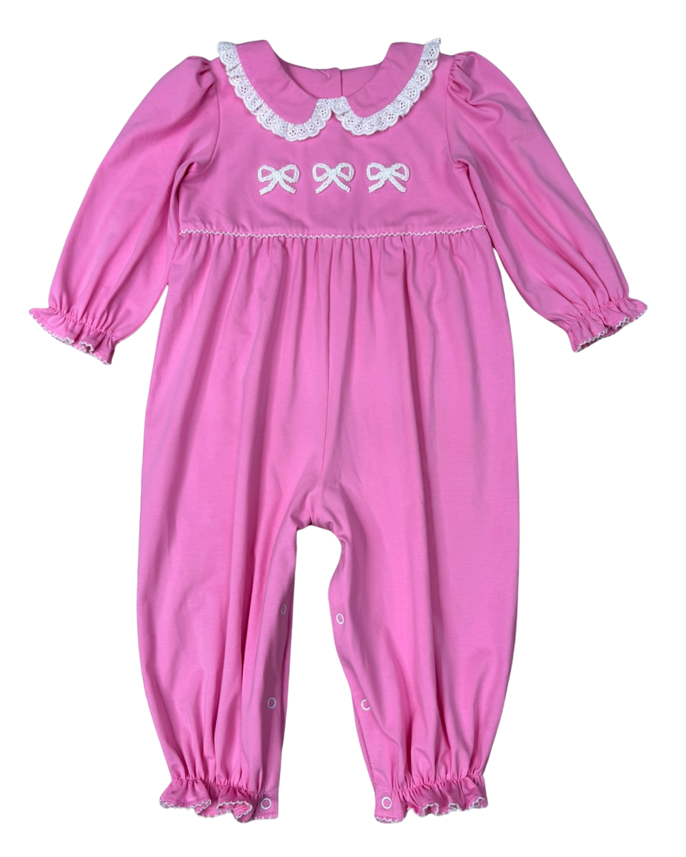 A pink long-sleeve baby jumpsuit with white lace trim on the collar, white embroidered bows on the chest, and ruffled trim on the leg cuffs, shown against a plain white background.