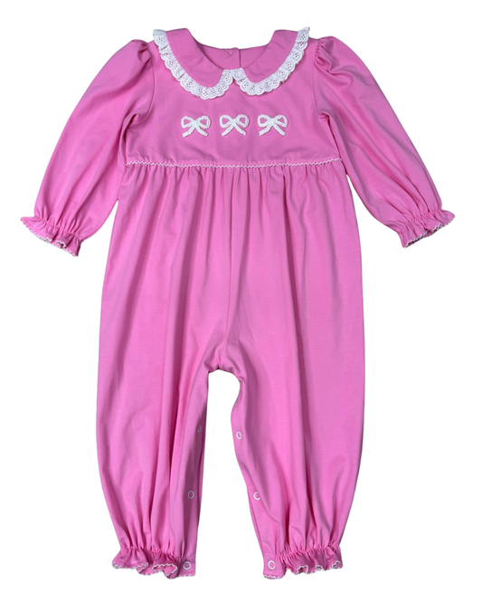 A pink long-sleeve baby jumpsuit with white lace trim on the collar, white embroidered bows on the chest, and ruffled trim on the leg cuffs, shown against a plain white background.
