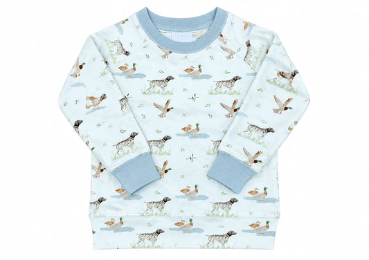 A long-sleeve baby sweatshirt featuring an all-over duck hunting print with dogs, ducks, and water elements on a cream background with solid light blue ribbed collar, cuffs, and hem.