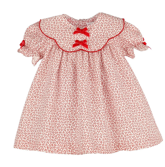 A baby girl's short-sleeve dress with a red and white floral print, featuring a large ruffled Peter Pan collar with red trim, two red bow accents at the neckline, and ruffled sleeves with red bows.