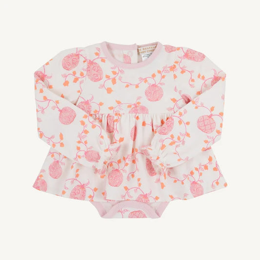 A baby long-sleeve top with a pink and orange berry vine pattern on a white background, featuring a ruffled peplum waist and tie detail, laid flat on a light cream background.