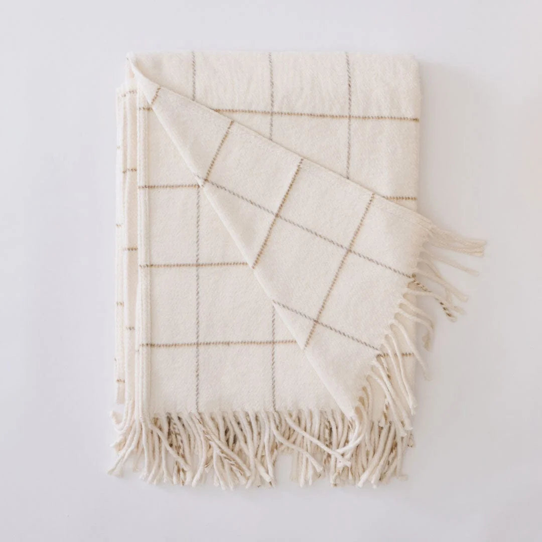 An off-white woven throw blanket with a tan windowpane grid pattern and fringed edges, folded neatly on a light gray background.