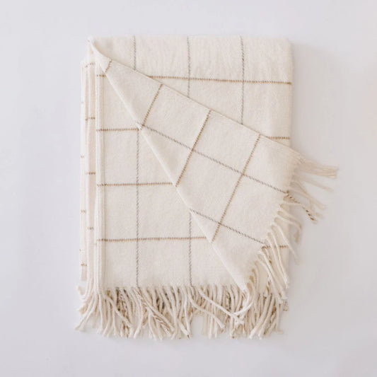 An off-white woven throw blanket with a tan windowpane grid pattern and fringed edges, folded neatly on a light gray background.