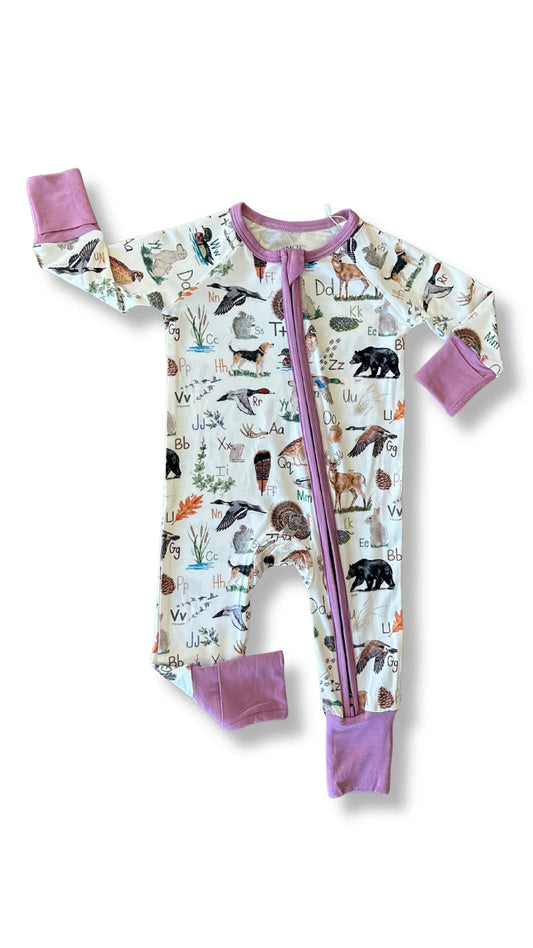 A baby's long-sleeve footed sleeper with a colorful animal and nature print on an off-white background, featuring solid purple cuffs, collar trim, and zipper.