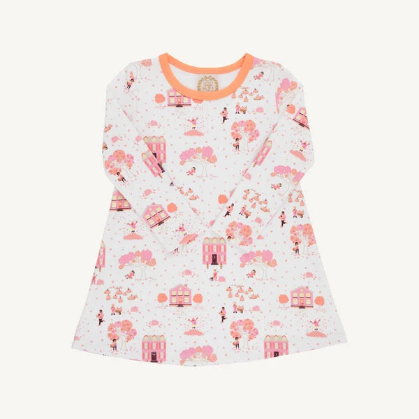 A long-sleeve baby dress with a white base, featuring a pink and orange whimsical print of trees, houses, and figures, finished with a solid orange crew neck.