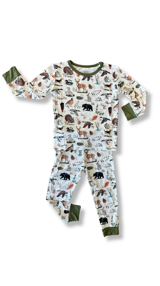 A two-piece children's pajama set featuring an all-over animal print on a white background, with sage green cuffs and collar trim, displayed on a clean white background.