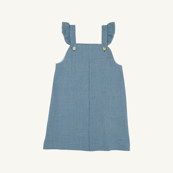 A blue tweed textured fabric pinafore dress with ruffled shoulder straps and small gold buttons, shown flat against a light cream background.