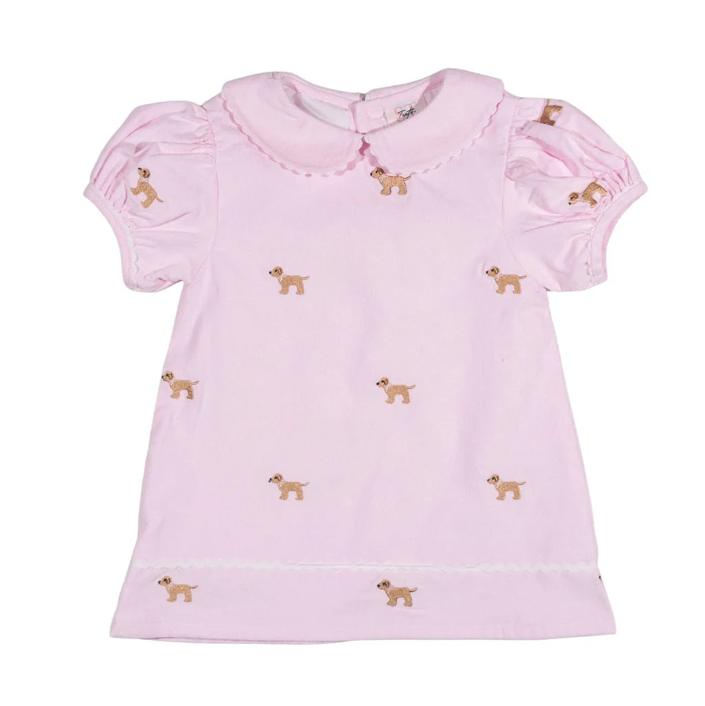 A light pink short-sleeve baby corduroy dress with a Peter Pan collar, featuring small embroidered brown dogs scattered across the front, set against a plain white background.