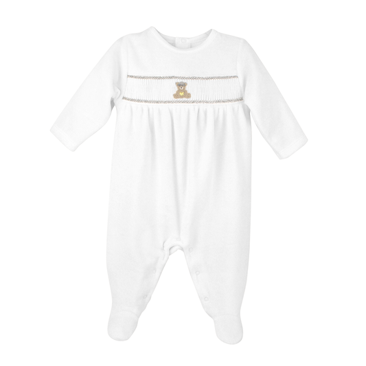 A white long-sleeve baby footed sleeper with smocked detailing across the chest, featuring a small embroidered teddy bear  and a decorative horizontal stripe.