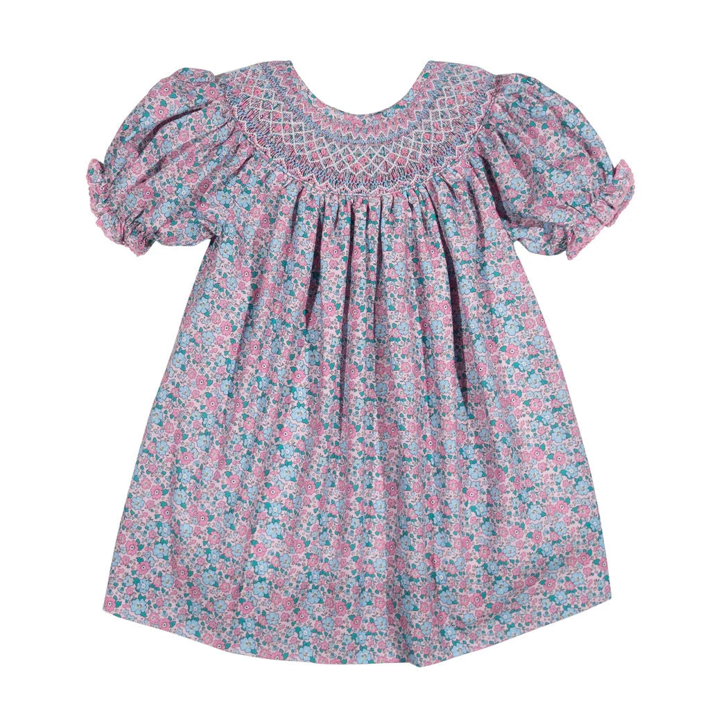 A toddler girl's dress with a pink, blue, and white floral pattern, featuring a smocked yoke and puffed short sleeves, shown against a plain white background.