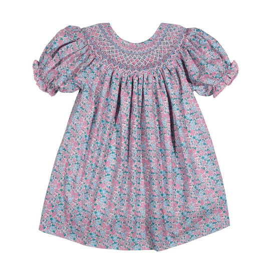 A toddler girl's dress with a pink, blue, and white floral pattern, featuring a smocked yoke and puffed short sleeves, shown against a plain white background.