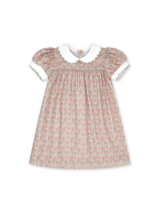 A toddler girl's short-sleeve dress with a dense multicolor floral print on a light beige background, featuring a contrasting white Peter Pan collar and white sleeve cuffs with delicate green trim.