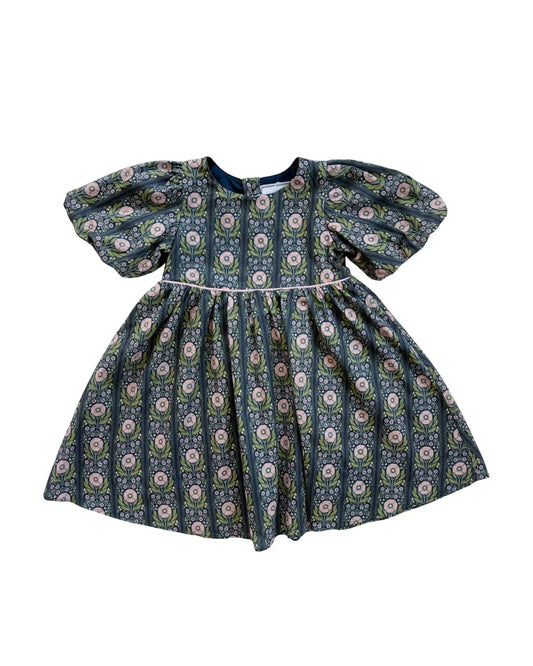 A toddler girl's dress with puff sleeves and a gathered skirt, featuring an all-over vertical floral pattern in navy blue, sage green, and pink on a white background.