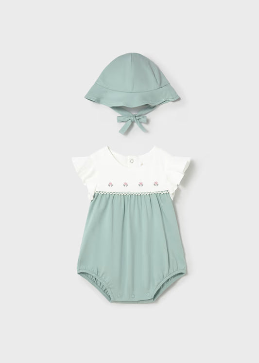 Baby girl romper with embroidered flowers on a cream bodice and a pale green bottom and matching hat.