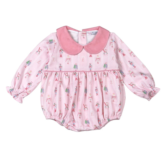A pink long-sleeve baby romper with a Peter Pan collar, featuring an all-over nutcracker and tree print, set against a plain white background.