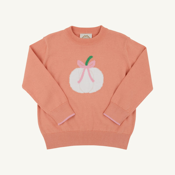 A peach-pink crewneck sweater featuring a white pumpkin graphic with a pink bow and green stem on the chest, displayed flat against a light cream background.
