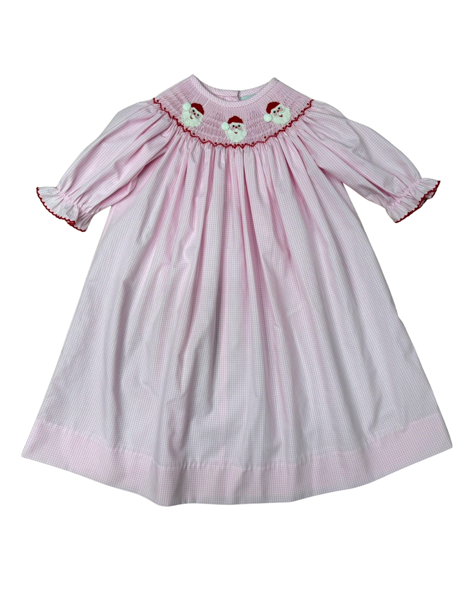 A pink and white gingham baby dress with smocked detailing at the collar, featuring embroidered Santa Claus faces and red trim, shown against a plain white background.