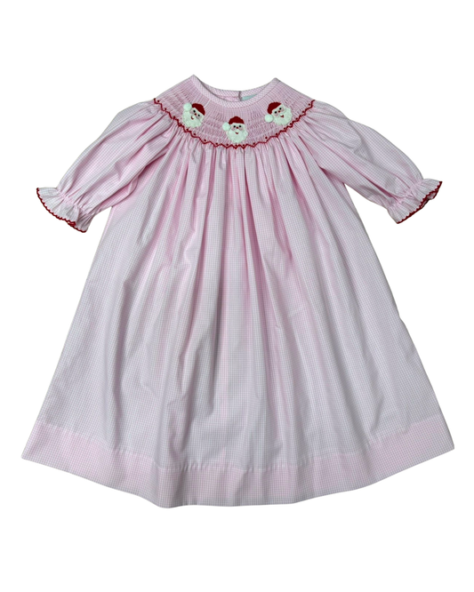 A pink and white gingham baby dress with smocked detailing at the collar, featuring embroidered Santa Claus faces and red trim, shown against a plain white background.