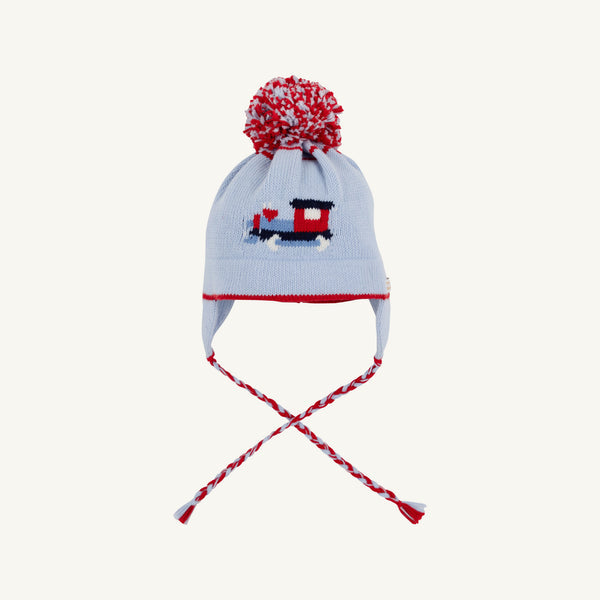A light blue knit winter hat with a red and white pom-pom, featuring a small red and navy train motif on the front and matching ear flaps with braided red, white, and blue ties.