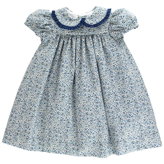 A baby girl's smocked dress featuring a blue and white floral print, with a navy blue Peter Pan collar and ruffled short sleeves, shown against a plain white background.