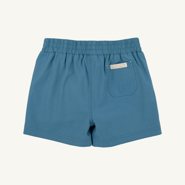 Blue elastic-waist shorts with a side pocket and a small white brand label, shown flat against a light cream background.