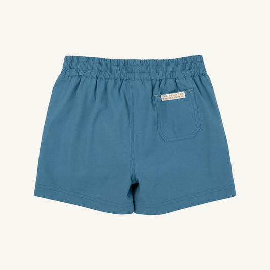 Blue elastic-waist shorts with a side pocket and a small white brand label, shown flat against a light cream background.