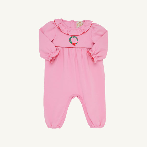 A pink baby jumpsuit with long ruffled sleeves, a ruffled collar, and a small embroidered green wreath with red berries on the chest, shown against a plain off-white background.