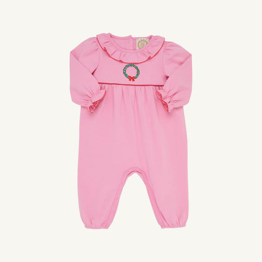 A pink baby jumpsuit with long ruffled sleeves, a ruffled collar, and a small embroidered green wreath with red berries on the chest, shown against a plain off-white background.