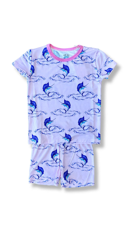 A two-piece girls' pajama set featuring a short-sleeve top and matching shorts in a light pink color, printed with a blue and white marlin and wave pattern. The top has a contrasting pink collar.
