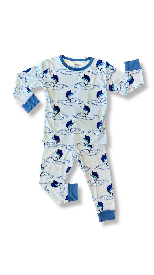 A two-piece children's pajama set featuring a long-sleeve top and matching pants with an allover blue and navy marlin print on a white background, finished with solid blue cuffs and collar.