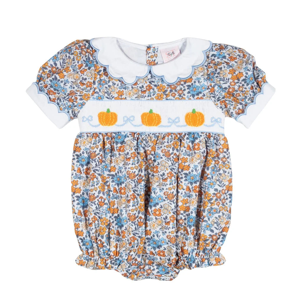A baby girl's short-sleeve bubble romper dress featuring a white Peter Pan collar, a smocked bodice with three orange pumpkins and blue bows, and a blue, orange, and white floral print.