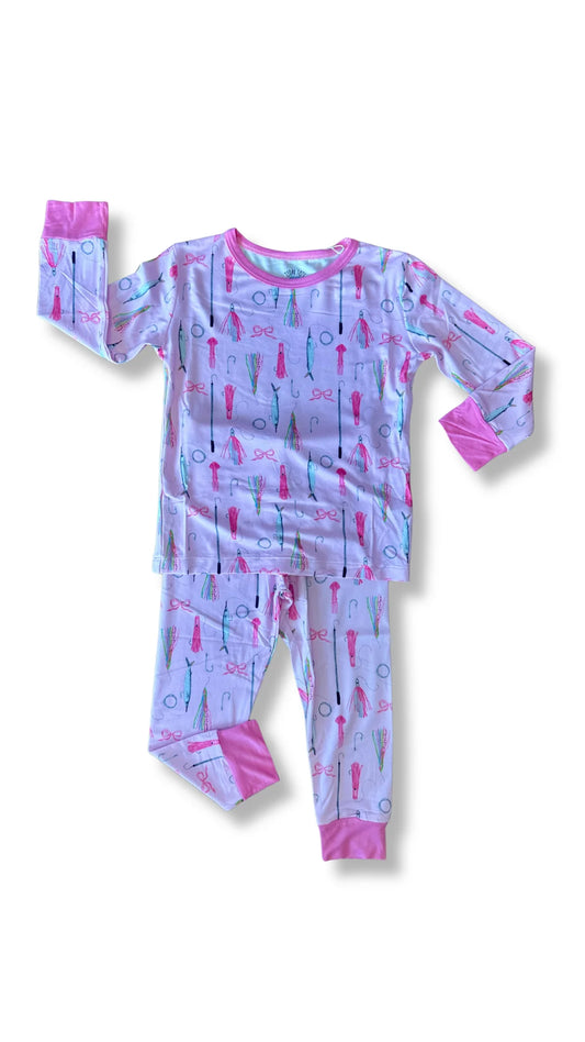 A two-piece children's pajama set featuring a long-sleeve top and matching pants in a light lavender-purple color, decorated with a whimsical print of pink, red, and blue fishing lures. The cuffs and collar of the top are solid pink, and the cuffs of the pants are solid pink.